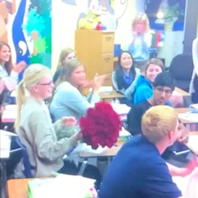 Carolyn holding a bouquet of red roses in class during the promposal